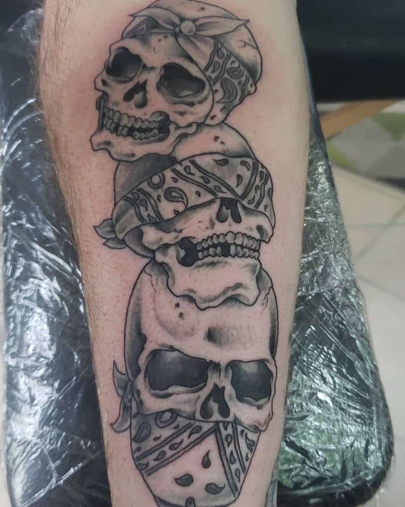 Tattoo of three skulls with bandanas covering eyes, mouth, and forehead on a leg
