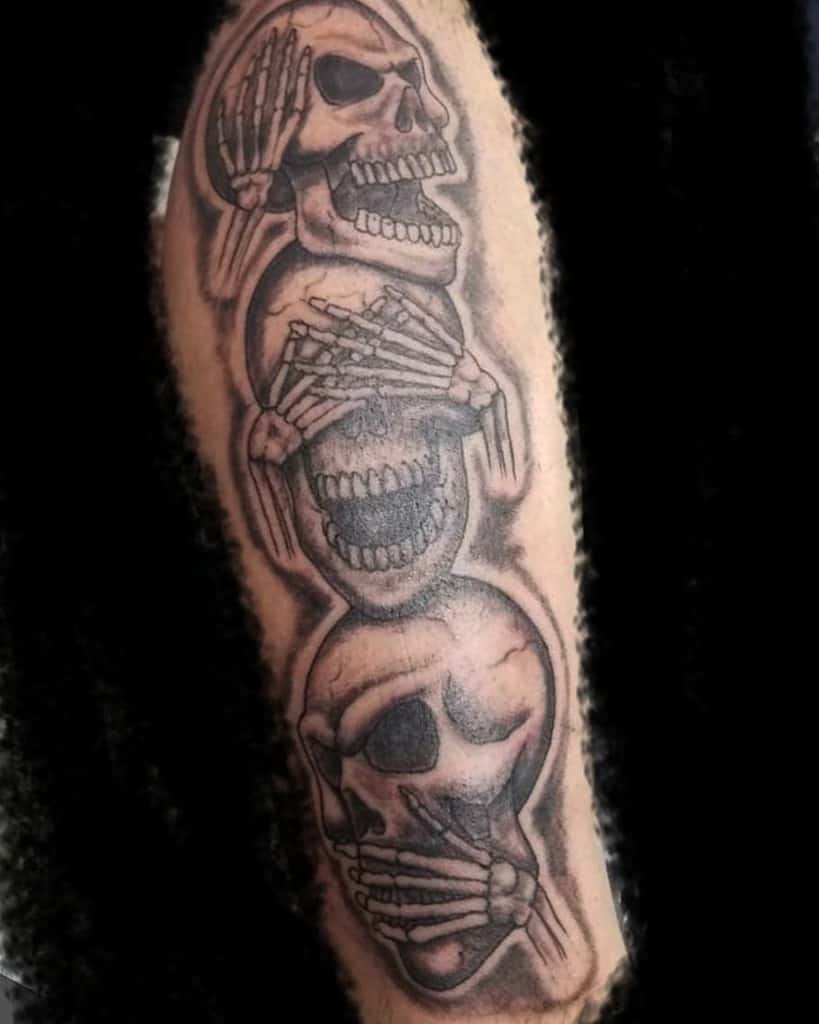 Tattoo of three skulls covering eyes, ears, and mouth on an arm, symbolizing "see no evil, hear no evil, speak no evil