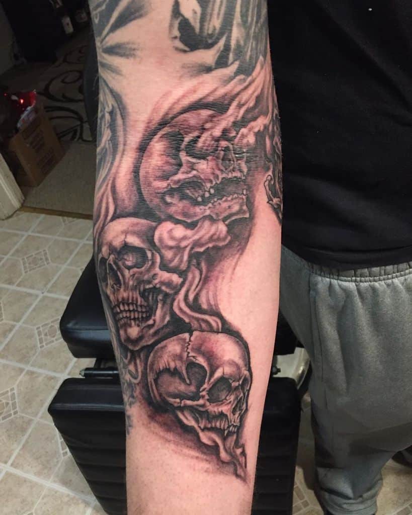 Forearm tattoo of three skulls with a smoky, flowing design, symbolizing 'Hear No Evil, See No Evil, Speak No Evil,' in dark shading and bold details