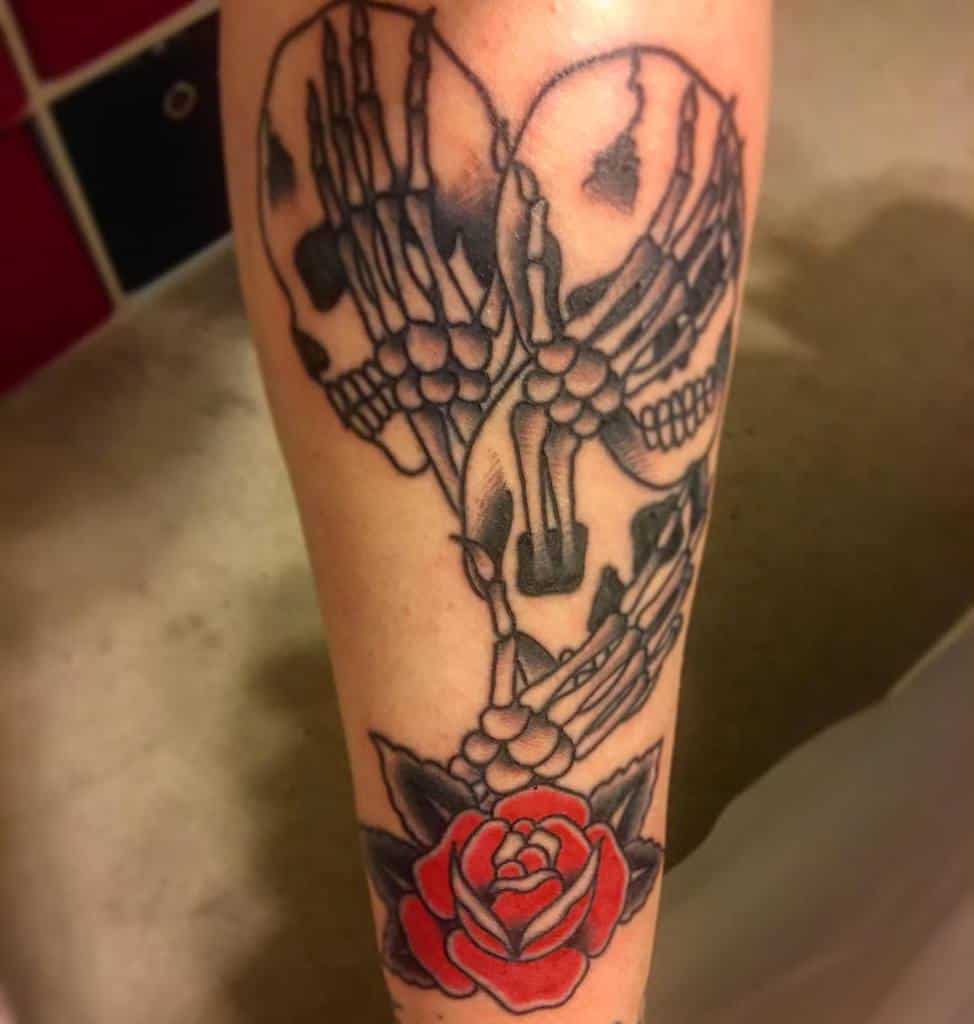 Tattoo featuring skeletal hands forming a heart shape with a red rose below, symbolizing love and mortality