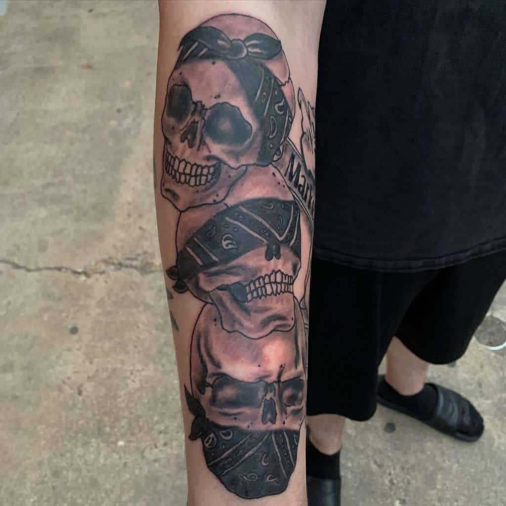 Black and gray tattoo of three skulls on a forearm, each wearing bandanas, symbolizing 'Hear No Evil, See No Evil, Speak No Evil,' with bold shading and fine details