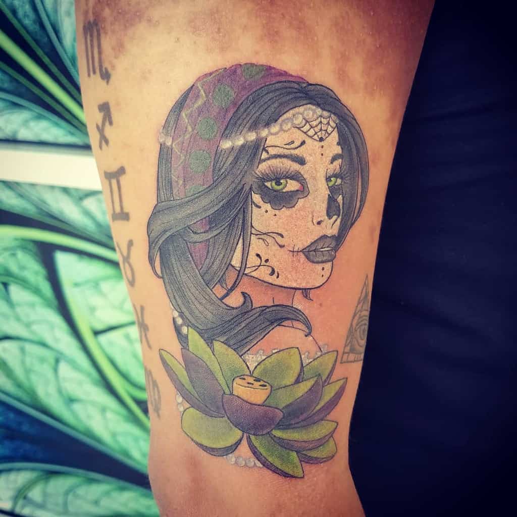 Colorful tattoo of a gypsy woman with Day of the Dead-inspired face paint, a lotus flower, and astrological symbols on the arm.