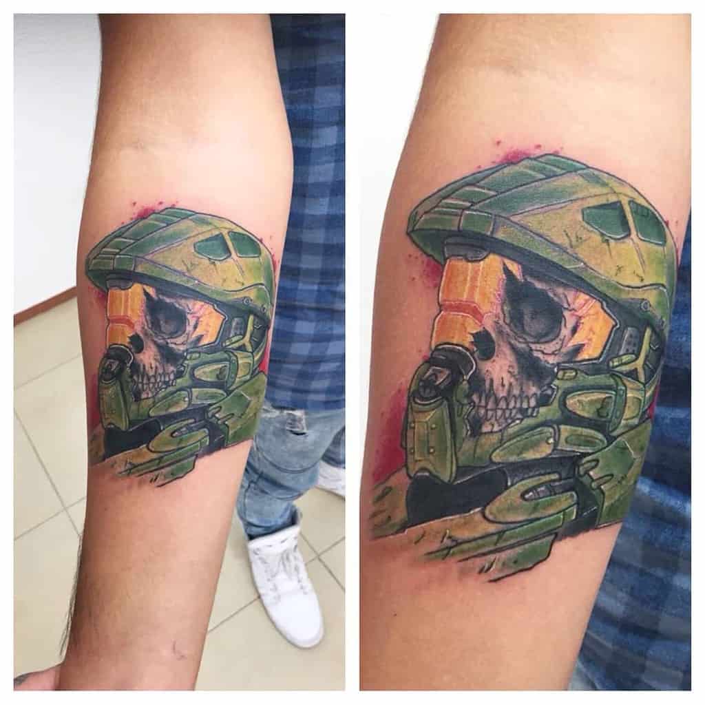 Dark and gritty Halo tattoo of Master Chief’s helmet revealing a skull inside, with a battle-worn look and splattered red details, inked on the forearm.