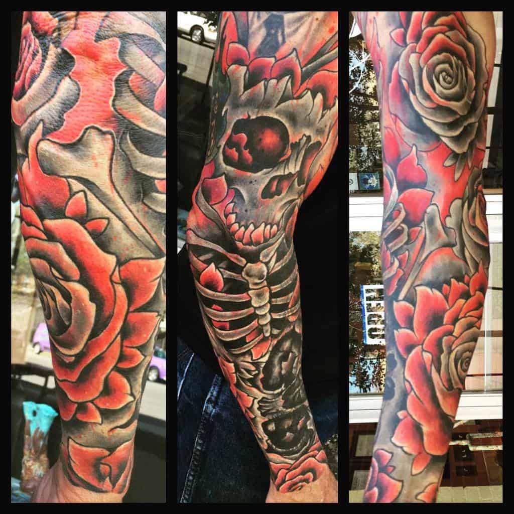 A bold full-sleeve tattoo combining bright red roses, a skeleton, and dark shading, blending surreal and dramatic elements for a striking visual effect