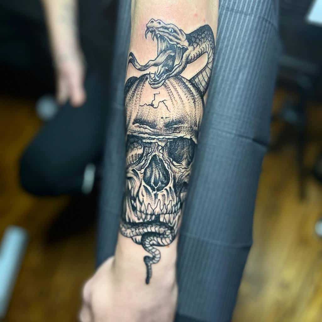 Tattoo of a skull with a snake emerging from it, located on a forearm