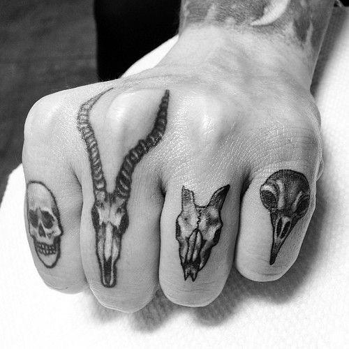A hand with tattoos of various skulls on the fingers