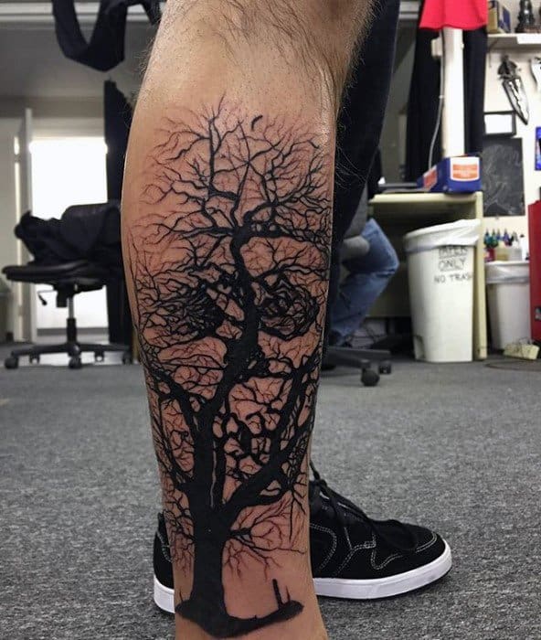 Calf tattoo of a dark tree with branches subtly forming a skull, while a lone figure sits beneath, adding a sense of solitude and mystery.