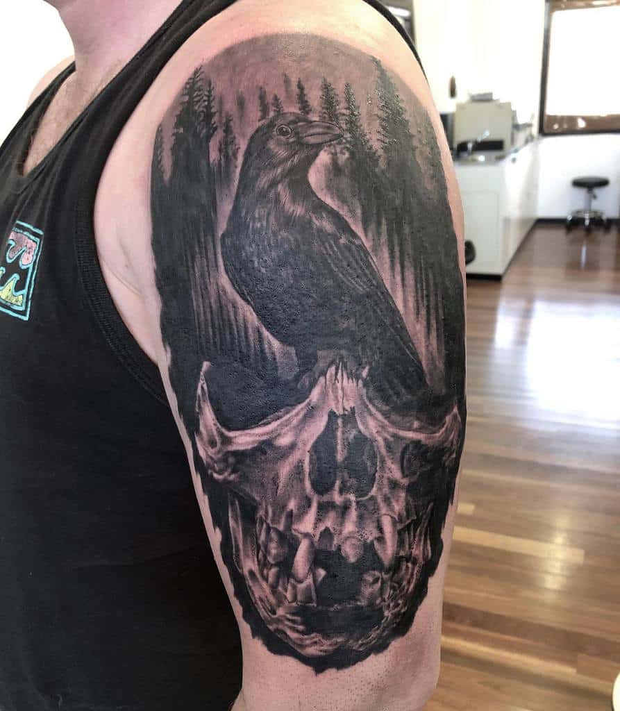 Tattoo of a raven on a skull with a forest background on an upper arm