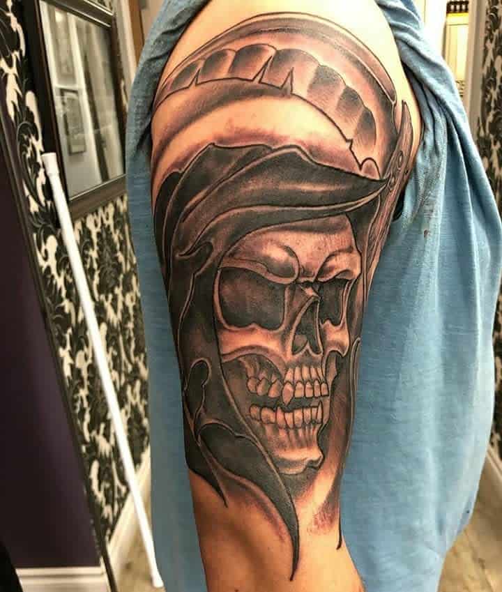 Upper arm tattoo featuring a detailed skull with a dark, menacing helmet, evoking themes of power, mystery, and death