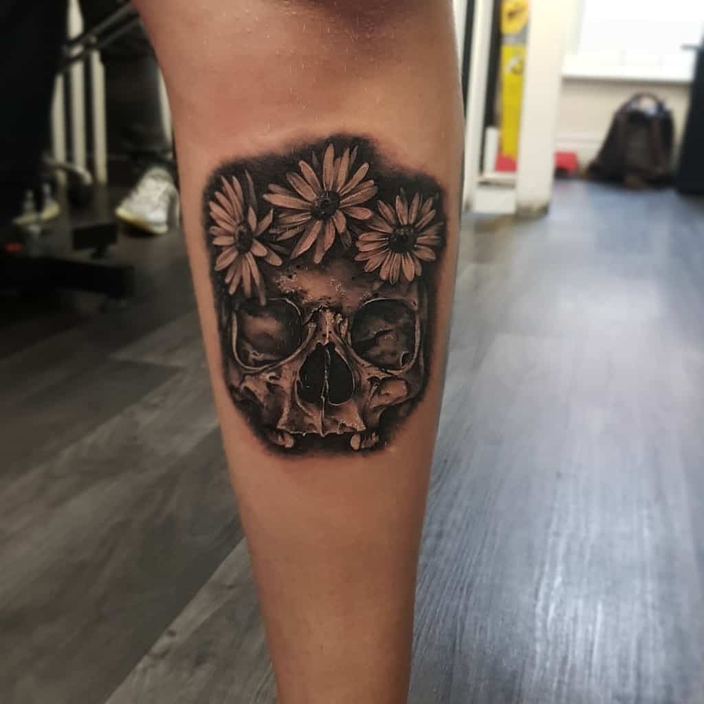 Calf tattoo realistic black and grey shading skull with a crown of daisies