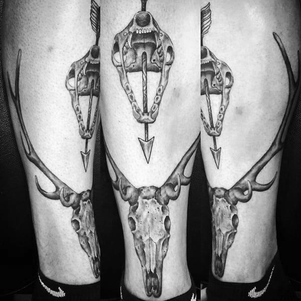 Black and grey leg tattoo featuring a broadhead arrow pointing down toward a detailed deer skull with large antlers on the calf.