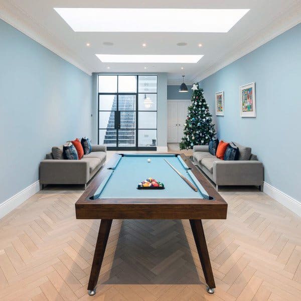 Bright basement with skylight ceiling, pool table, modern sofas, and a decorated Christmas tree.