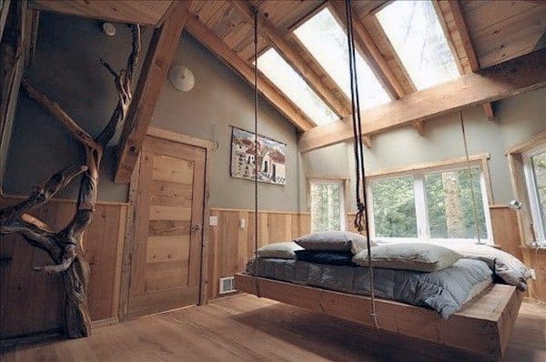 Rustic hanging bed in a cozy bedroom with wood-paneled walls, skylights, and natural accents.