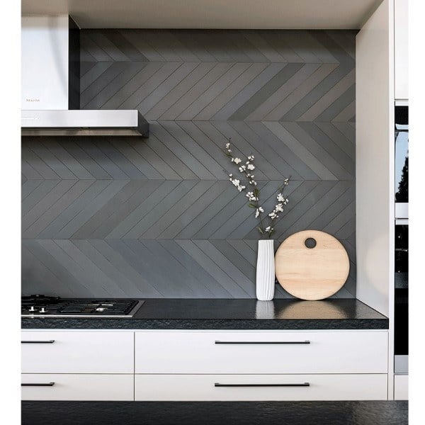 Modern kitchen with slate gray chevron tile backsplash, black countertop, and white cabinets.