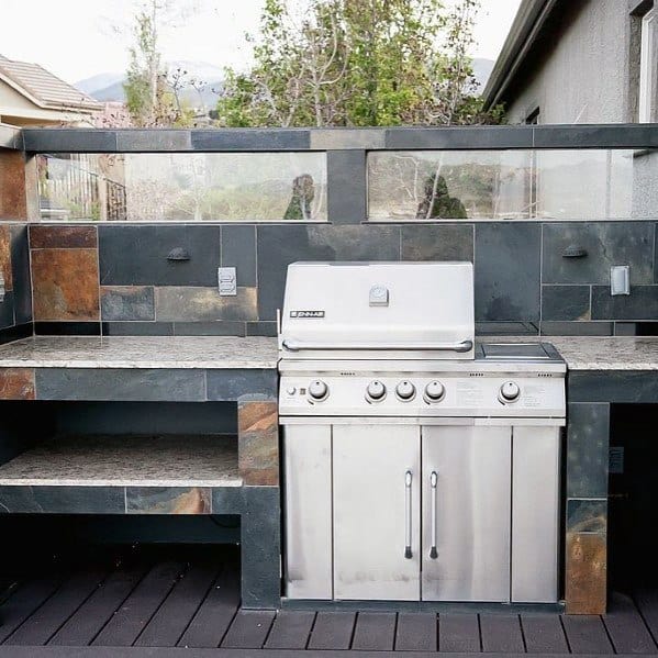 Outdoor kitchen with built-in stainless steel grill, stone countertops, and slate tile backsplash