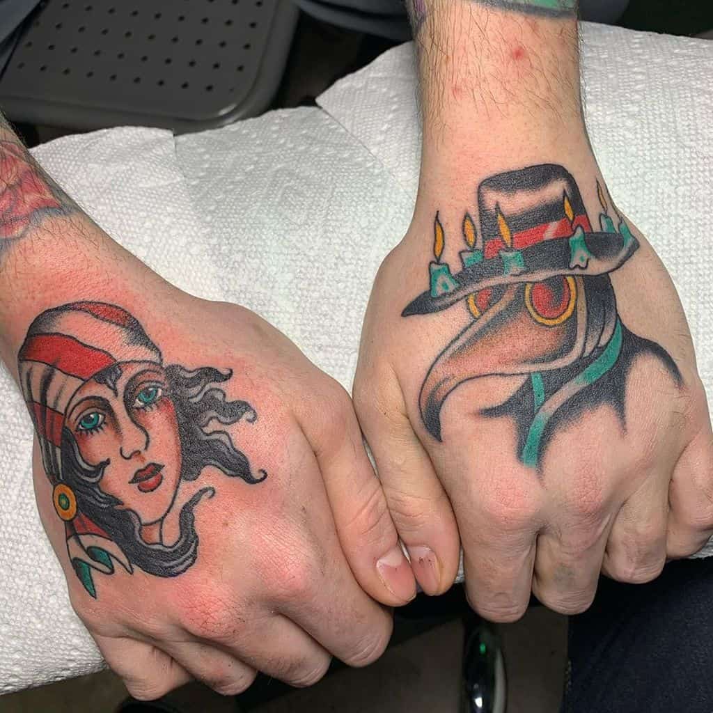 Colorful traditional tattoos on both hands: a gypsy woman with flowing hair and a red headscarf on one, a plague doctor with a candle-lit hat on the other.