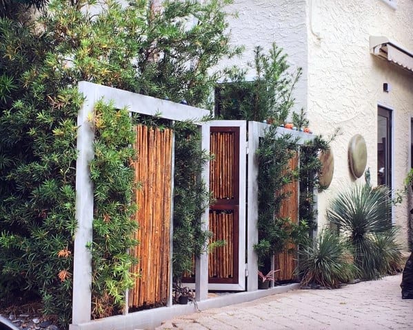 Metal-framed bamboo fence with gate, surrounded by lush shrubs, in a serene and sophisticated outdoor oasis.