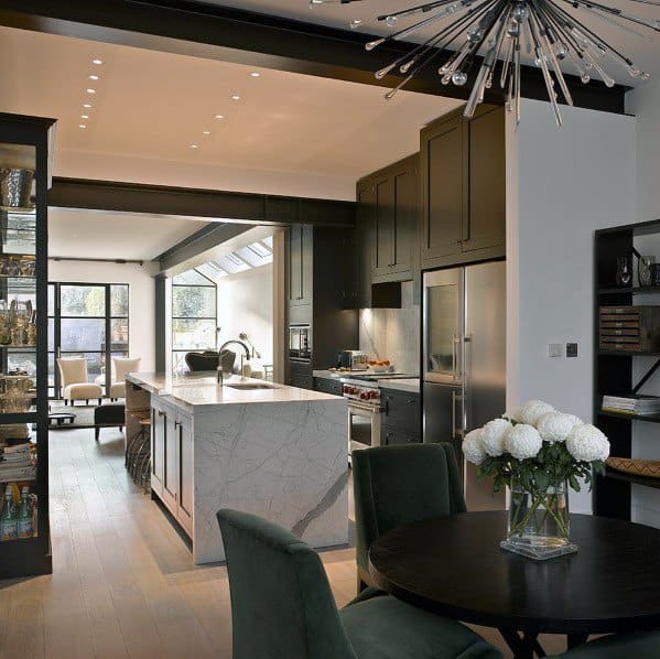 Luxurious black kitchen with marble island, green chairs, and modern lighting fixture.