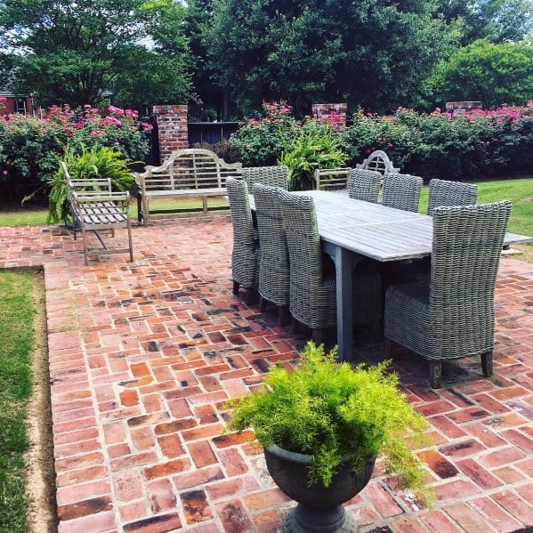 Brick-floored patio with dining table, chairs, benches, and lush greenery
