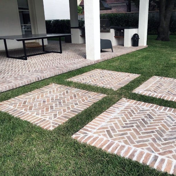 Walkway patio with geometric brickwork, grass, and a table under a covered area