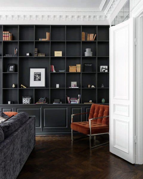 Sleek black built-in bookcase with open shelving and lower storage cabinets, paired with a bold orange armchair and herringbone wood flooring for a modern, sophisticated living space