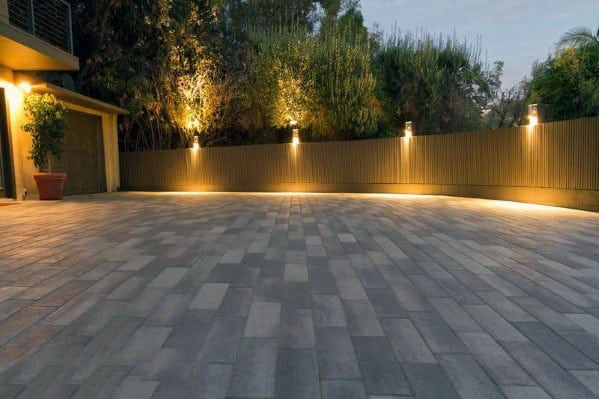 Modern driveway with sleek, strategically placed lighting fixtures along the fence, highlighting the paved path and surrounding greenery at night