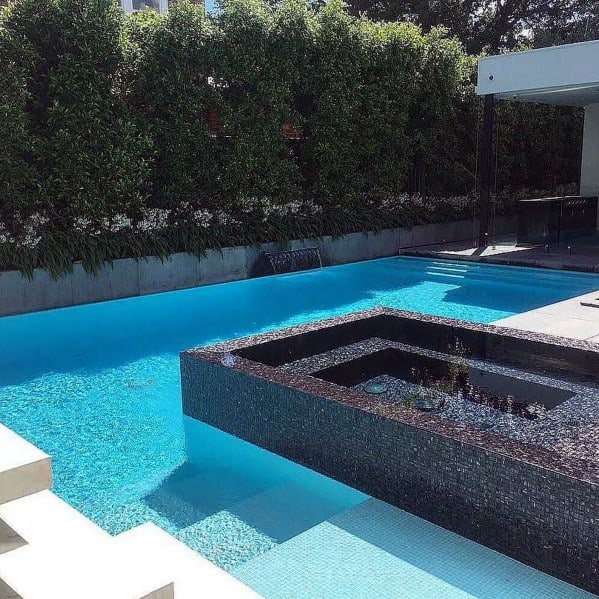Modern pool with turquoise tiles, black iridescent spa feature, and lush privacy hedges.