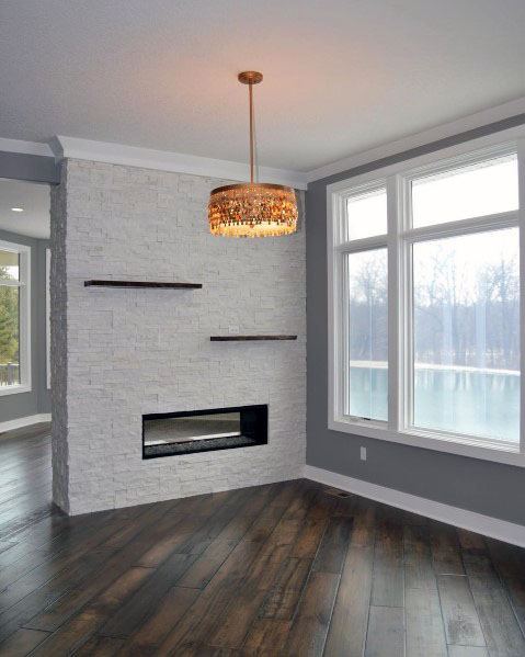 Modern room with a stacked stone wall, fireplace, and large windows overlooking a lake