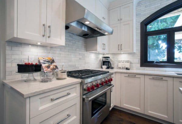 Modern kitchen with white cabinetry, subway tile backsplash, stainless steel range hood, and bold red stove knobs