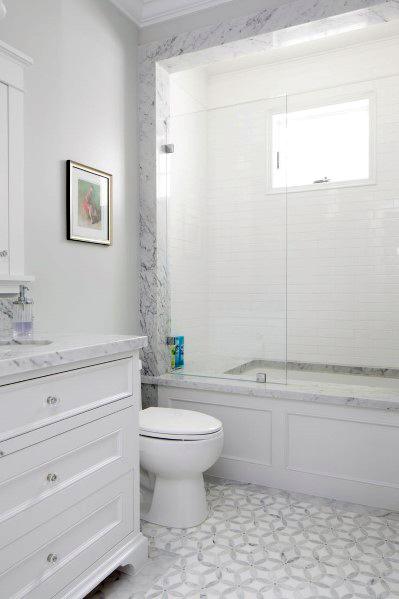 White bathroom boasting a marble shower, toilet, patterned floor, and framed art on the wall