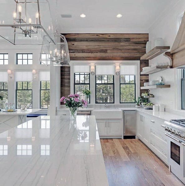 White kitchen with marble countertops, wood accent wall, open shelving, and elegant lighting.
