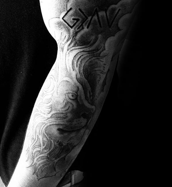 Forearm tattoo featuring "God is greater than the highs and lows" symbol with a detailed lion and cloud design