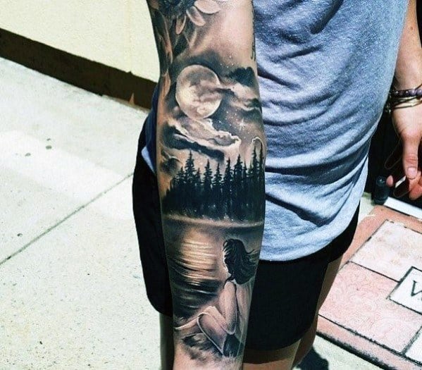 Forearm tattoo in black and grey showing a woman sitting by a lake, gazing at a full moon over pine trees and a softly lit night sky.