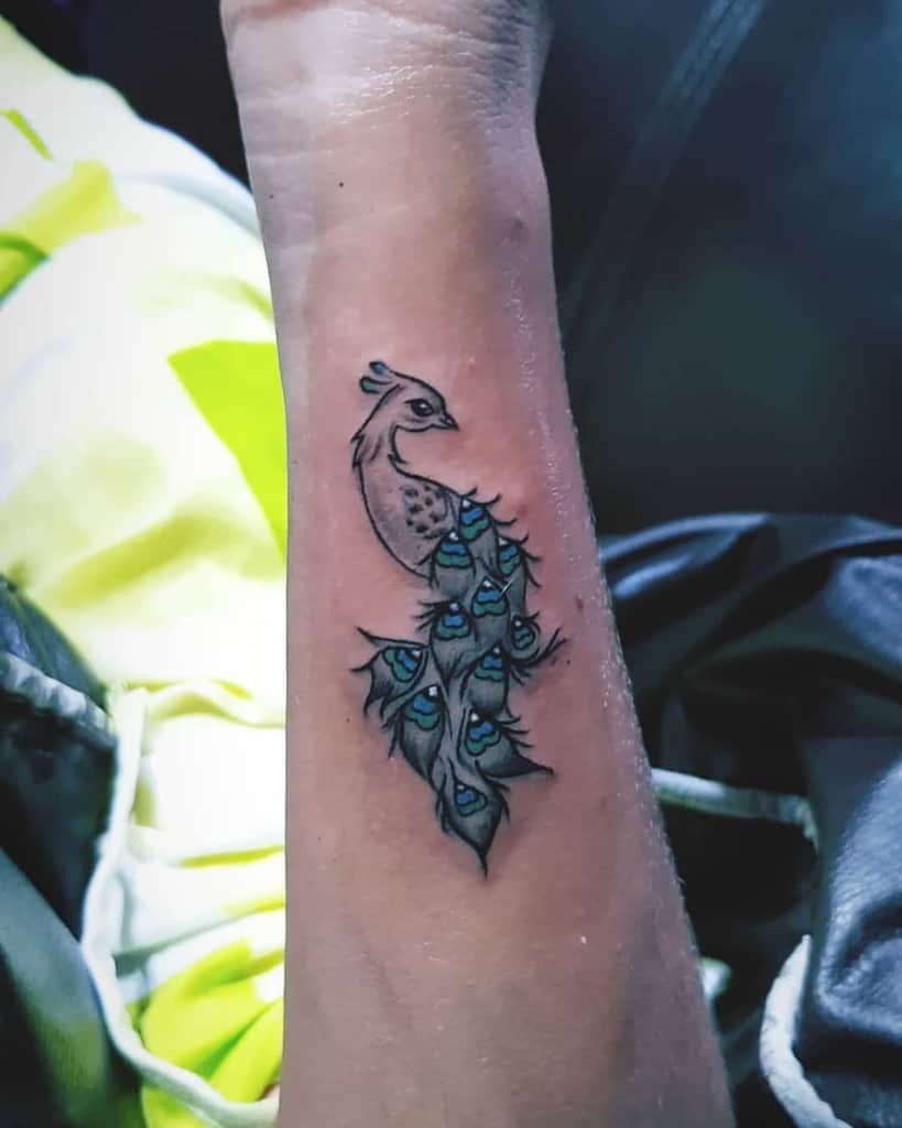 Small peacock tattoo with a delicate tail of blue and green feathers, placed on the forearm.