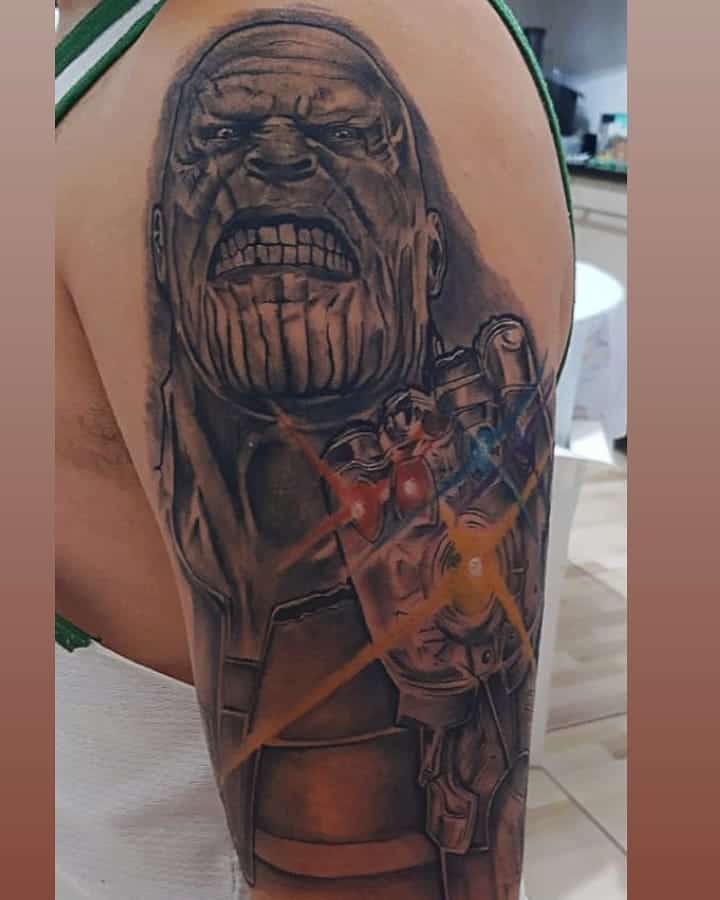 A black and gray tattoo of Thanos with an intense expression, featuring the Infinity Gauntlet and glowing stones, with bursts of light