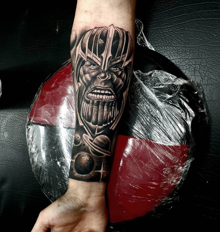 A black and gray tattoo of Thanos' face, detailed helmet, and planets surrounding the Infinity Gauntlet