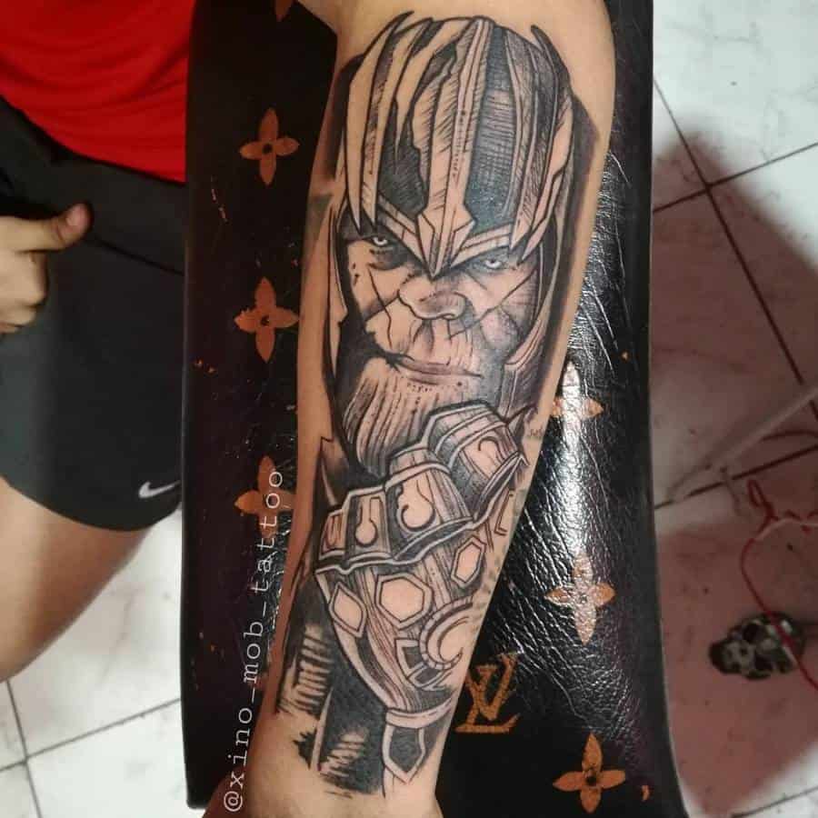 A black and gray tattoo of Thanos, with detailed shading on his face and helmet, and the Infinity Gauntlet on his arm