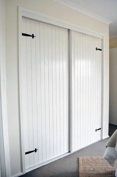 White sliding barn-style closet doors with black hinges in a cozy carpeted closet