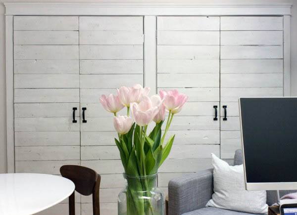 A charming whitewashed sliding closet door with a rustic slatted design, paired with a fresh vase of pink tulips for a light, airy feel