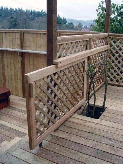 Wheeled wooden gate with lattice design, shielding a tree in the deck
