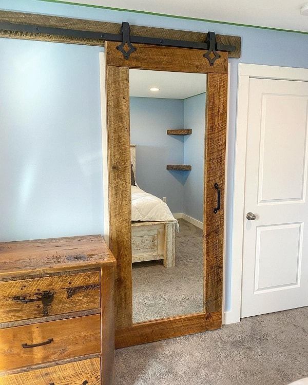 Sliding barn door with a full-length mirror in a rustic bedroom.