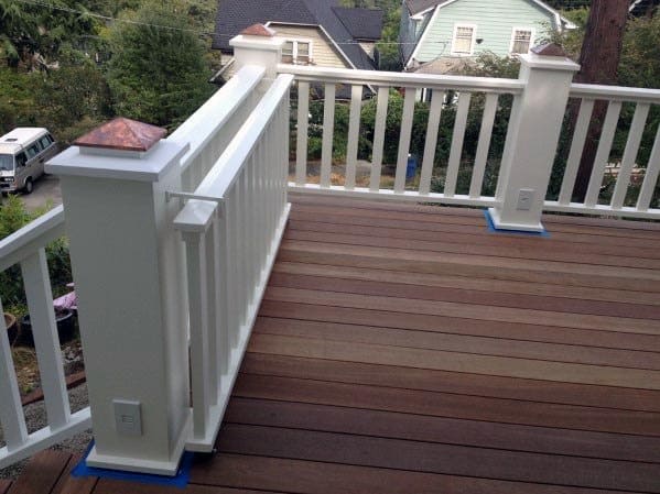 Wooden deck with white railing and gate, overlooking trees and houses
