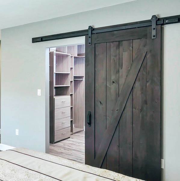 Dark wooden barn door on a sliding rail, opening to a sleek closet with modern shelves and drawers