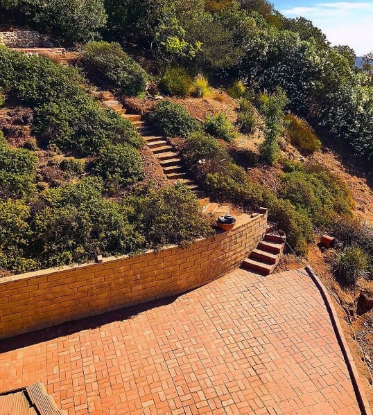 A sunlit, terraced garden with brick paths and steps nestled in lush greenery