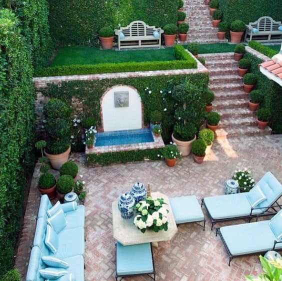 Elegant garden with brick steps, a fountain, seating, and lush greenery
