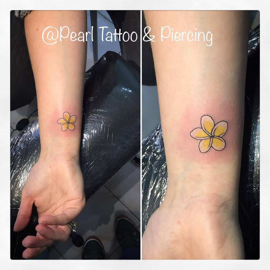 A tattoo of a vibrant yellow plumeria with a bold black outline graces a person's forearm