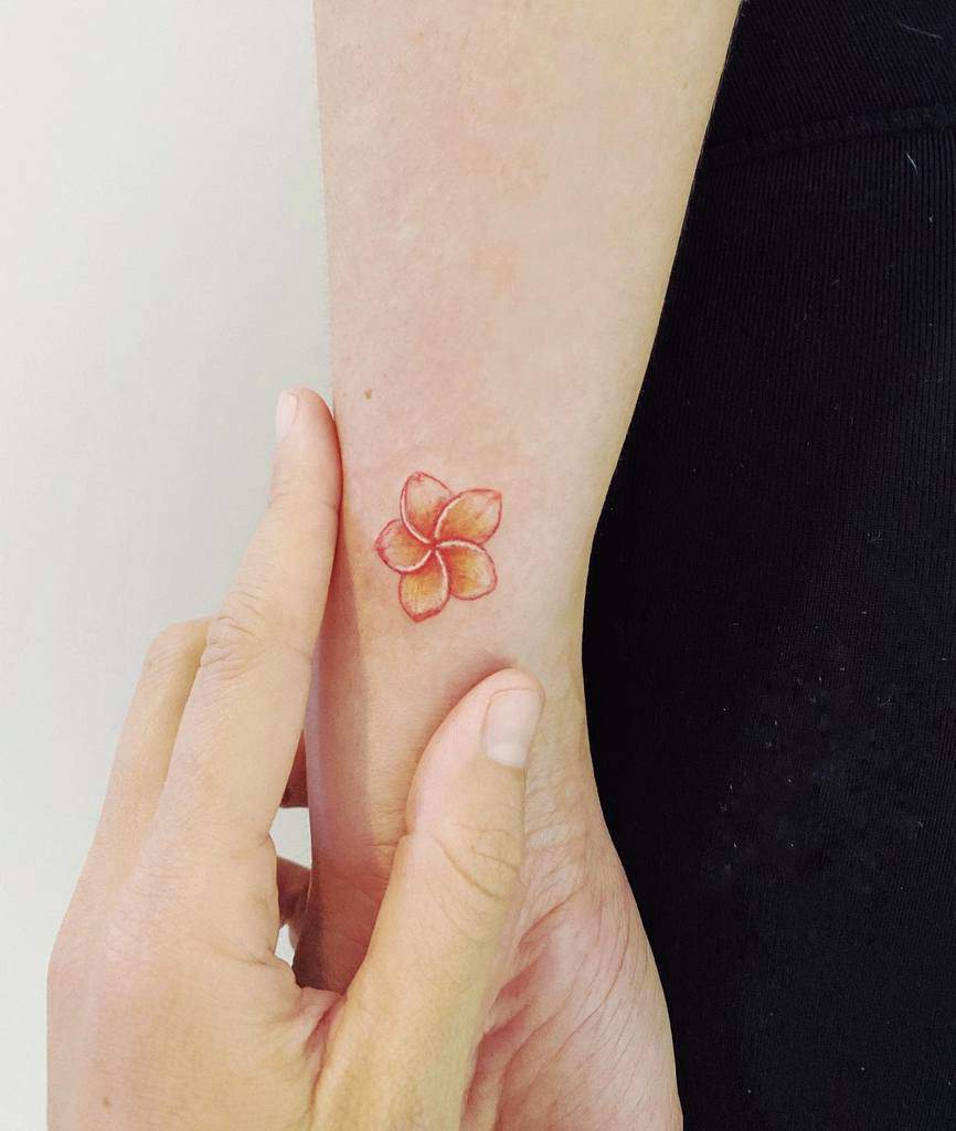 Small, colorful plumeria tattoo on an arm