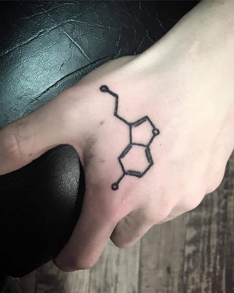 A tattoo of the serotonin chemical structure adorns the back of a person's hand, symbolizing happiness and well-being