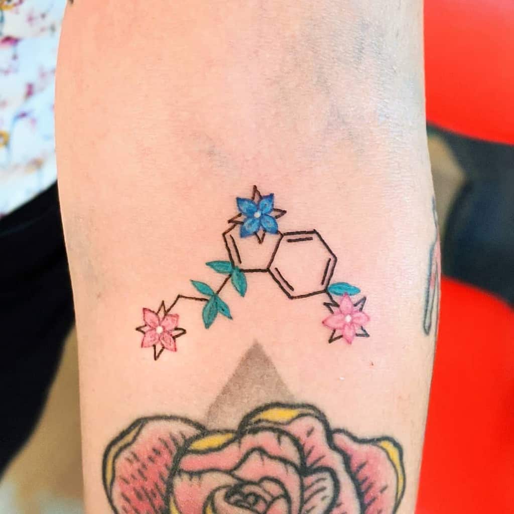 A serotonin molecule intricately inked on the person's arm, surrounded by delicate blue and pink flowers