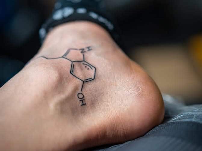 A foot with a serotonin chemical structure tattoo on an ankle